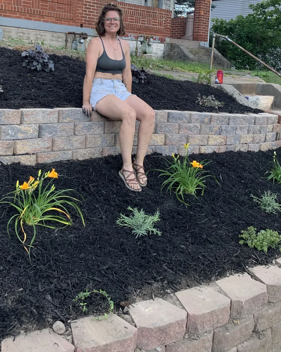 Katy seated on a retaining wall among newly planted black-mulch garden beds in Pittsburgh, Pennsylvania